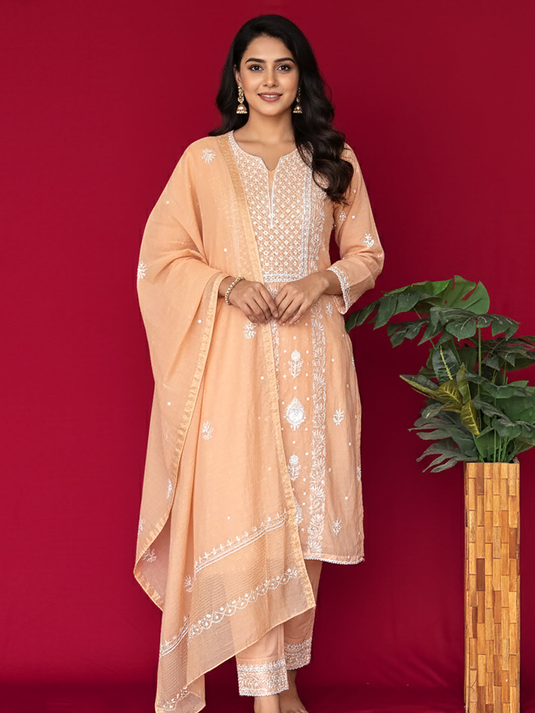 Woman wearing a peach chikankari outfit with white embroidery against a red background