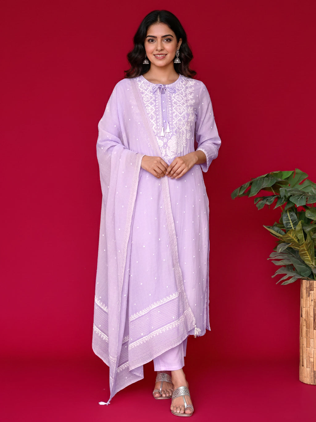 Woman wearing a light purple chikankari outfit with white embroidery against a red background