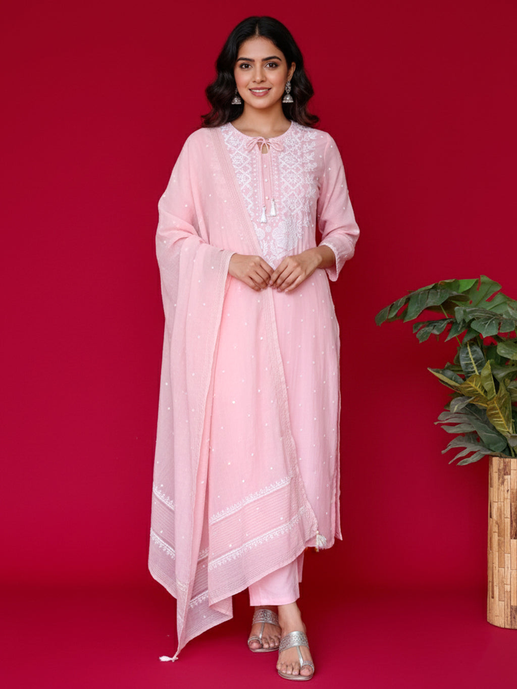 Woman wearing a pink chikankari outfit with white lace details on a red background